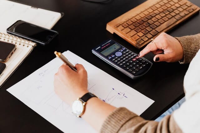 Person using a calculator and taking notes at a desk